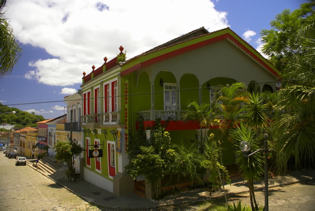 Rua de pedras em declive com casario colorido e vegetação tropical em Antonina