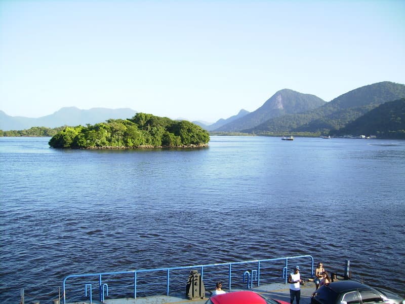 Foz da Baía de Guaratuba com pequena ilha arborizada, águas azuis e montanhas ao fundo