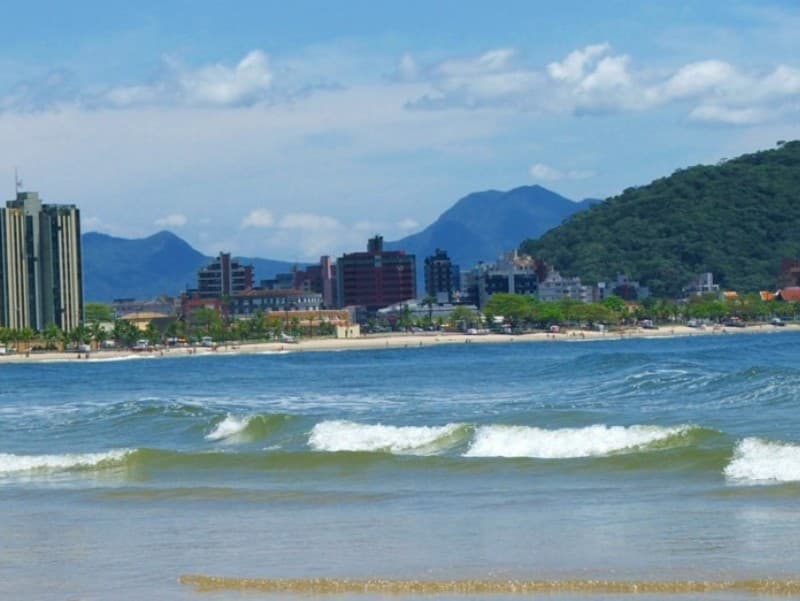 Praia Central de Guaratuba com mar calmo, orla urbana, banhistas e morros ao fundo