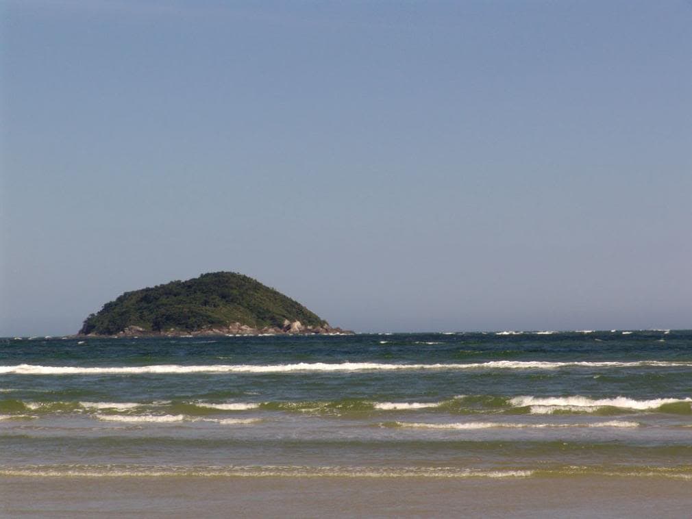 Praia de ondas calmas com a silhueta da Ilha do Mel ao largo